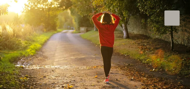 Thumbnail of person walking on a tree-lined path with hands on their head.