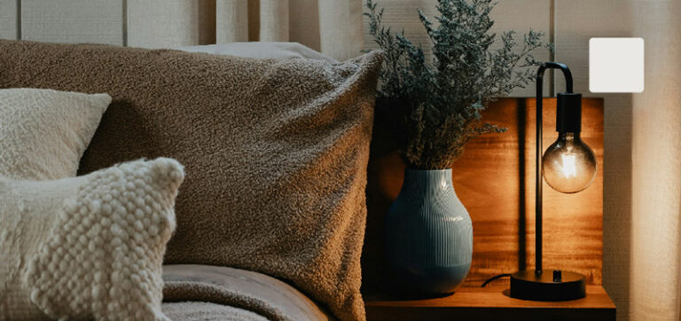 Thumbnail of a bed beside a table with a light and flowers.