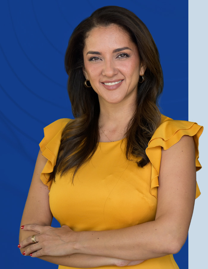 Su agente de seguros! Mujer sonriente vestida de amarillo y con los brazos cruzados, frente a un rectángulo azul. Your insurance agent! Smiling woman in yellow with arms crossed against a blue rectangle.